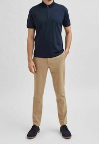 Námořnická polokošile s krátkým rukávem a zipovým límcem, v kombinaci s béžovými chinos kalhotami a tmavě námořnickými botami. Hladká textura a přizpůsobivý střih.