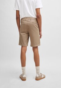 Shorts beiges en mélange de coton, avec une coupe régulière, des poches arrière et des bords ourlés, associés à un t-shirt blanc uni et des baskets beiges.