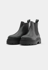 Bottines en cuir noir avec panneaux élastiques sur les côtés, bout rond et semelle en caoutchouc épaisse et chunky avec des détails de relief.