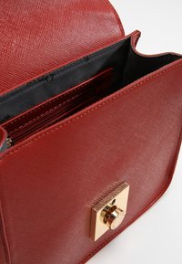 Červená texturovaná kabelka se zlatými prvky, která má čtvercové zapínání. Interiér je podšitý černou látkou s přepážkami.