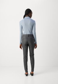 Lichtblauw lange mouw top gecombineerd met donkergrijze aansluitende broek. De broek heeft twee achterzakken en een gladde textuur. Zwarte hoge hak sandalen.
