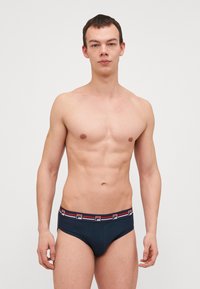 Slip blu navy con un design aderente, caratterizzati da una coulisse decorata con righe rosse e bianche. Tessuto morbido e elasticizzato per il massimo comfort.