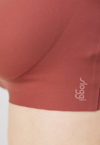 Sloggi-bh i dyp rød, laget av glatt stretchstoff. Har en sømløs design og subtil logo på siden.