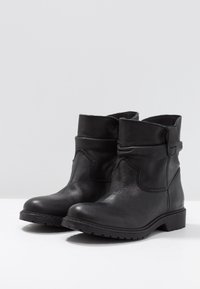 Czarne skórzane botki z teksturowanym wykończeniem, zaokrąglonym noskiem, niskim klockowym obcasem i dekoracyjnym szwem wzdłuż boku.