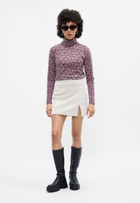 Top de cuello alto de manga larga con estampado floral en rosa y blanco, combinado con una mini falda crema con una abertura lateral y botas altas de cuero negras.