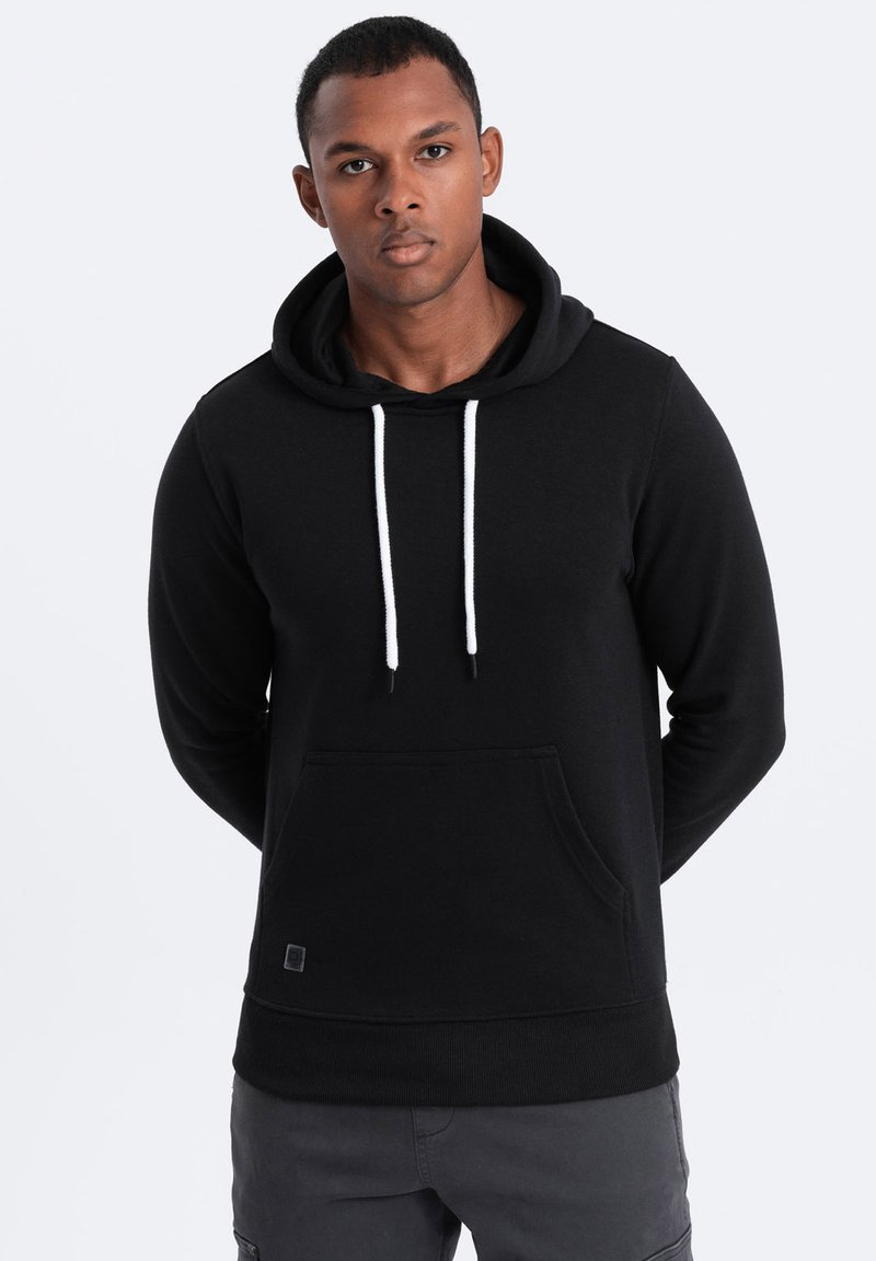 Sudadera negra hecha de un tejido suave, con un bolsillo frontal, cordones blancos y un dobladillo acanalado. Diseño simple y versátil.