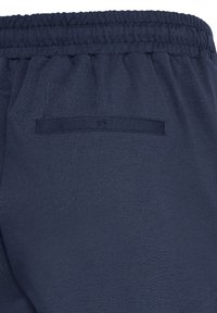 Pantalon à taille élastique bleu marine avec une seule poche passepoilée à l'arrière et un détail de couture visible.