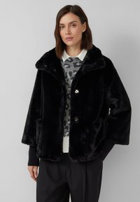 Veste en fausse fourrure noire avec un col châle, deux poches latérales et deux boutons. Associée à un pull gris à imprimé léopard et un pantalon noir.