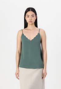 Green scalloped cami top with thin straps, made of smooth fabric, featuring a deep V-neckline and a relaxed fit.