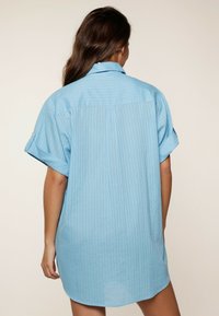 Jasnoniebieska koszula z krótkimi rękawami, z podwiniętymi rękawami, z delikatnymi pionowymi paskami i zaokrąglonym dołem.