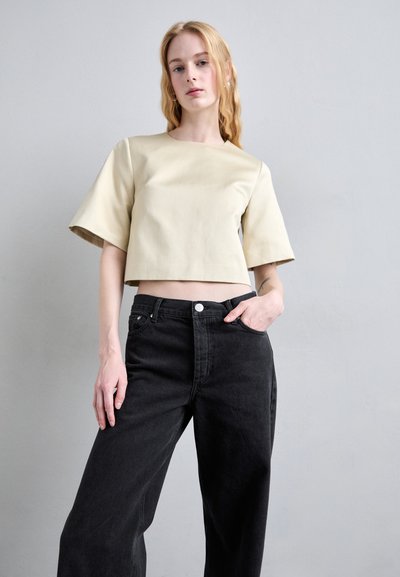 Light beige crop top with short sleeves, paired with high-waisted black wide-leg jeans. Smooth texture, minimal stitching, and classic button closure.