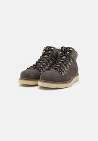 Botas de senderismo de ante gris oscuro con un cuello acolchado, suela blanca resistente y cordones negros con gancho y ojales de metal.