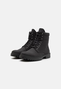 Botines negros hasta el tobillo hechos de tela texturizada, con ojales de metal, cordones y una suela robusta para mayor agarre y durabilidad.