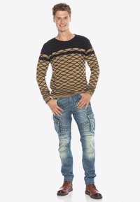 Brauner und schwarzer gemusterter Strickpullover mit geometrischen Designs, kombiniert mit hellblauen Cargo-Jeans, die mehrere Taschen und Akzente aufweisen.