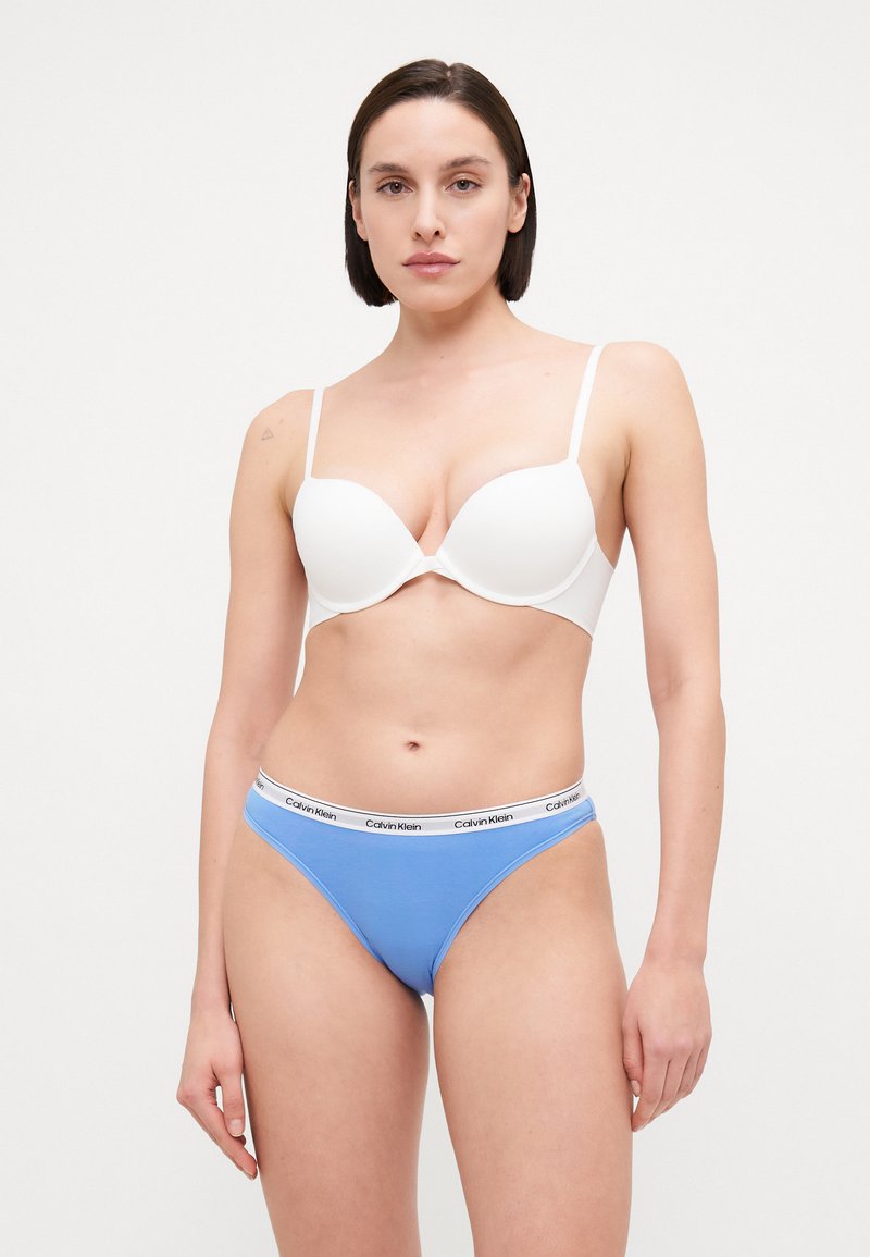 Reggiseno imbottito bianco con spalline regolabili; perizoma azzurro chiaro con cintura "Calvin Klein" in bianco e nero. Tessuto liscio, design minimal.