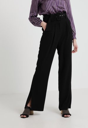 Zwarte wijde broek met zijsplitten, hoge taille en een bijpassende riem. Gecombineerd met een paarse gestreepte blouse met knopen en zwarte sandaaltjes met bandjes.