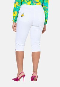 Pantaloni capri bianchi con tasche posteriori decorate con ricami di limone, fessure laterali all'orlo, abbinati a scarpe con tacco rosa.