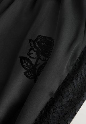 Czarny materiał sukienki z kwiatowym wzorem czarnej róży, z teksturowaną koronkową lamówką na krawędzi, tworzącą warstwowy projekt.