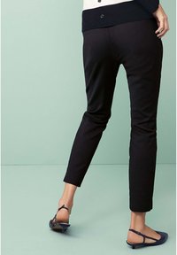 Pantalons noirs jusqu'aux chevilles avec une texture lisse associés à des ballerines navy à brides. Conception minimaliste, sans motifs ni éléments de quincaillerie visibles.