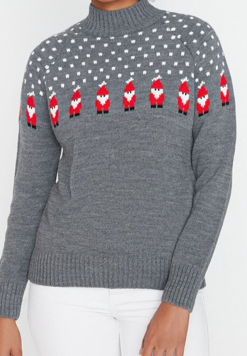 Maglione grigio lavorato a maglia con una fila di piccoli pupazzi di Babbo Natale rossi e bianchi sul petto e sulle spalle, indossato con pantaloni bianchi.