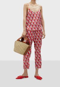 Kvinna som bär en färgglad geometrisk mönstrad linne och byxor, håller en vävd korghandväska och röda slip-on spetsiga skor.