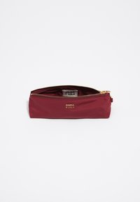 Neceser burdeos hecho de tela suave, con un zipper dorado y un logo grabado en la parte frontal. Forma compacta y rectangular.