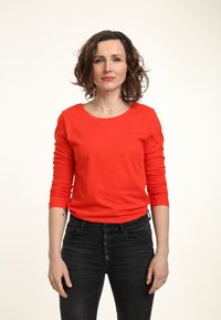 Maglietta rossa a maniche lunghe in cotone con scollatura rotonda e design aderente, abbinata a jeans neri a vita alta con chiusura a bottone.