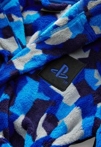 Blå och marinblå fleecekappa med geometriskt mönster, mjuk struktur och en svart PlayStation-logotyp patch. Dragkedja fram.