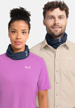 Vrouw in een paars Jack Wolfskin-shirt en man in een beige Jack Wolfskin-jas, beiden met marineblauwe nekverwarmers.