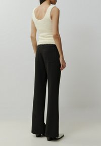 Fluffy crèmekleurig tanktop met een brede scooprug, gecombineerd met hoog-waisted zwarte broek met een rechte pijp en achterzakken.