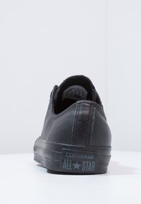 Fekete Converse sportcipő, textúrált bőr felsőrésszel, alacsony profilú és párnázott bokával. Gumitalppal rendelkezik, és dombornyomott "All Star" felirattal rendelkezik.