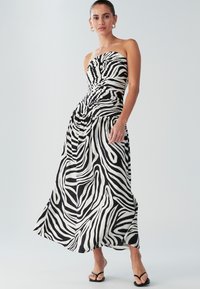 Rihmatu must-valge zebra-mustri kleit, millel on voltidega bodice, voolav seelik ja kerge kangas. Lamedad mustad sandaalid.