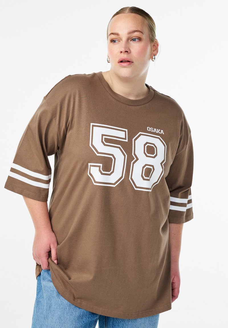 Rjava prevelika majica s kratkimi rokavi z belim potiskom številke "58" in besede "OSAKA", z belimi črtastimi poudarki na kratkih rokavih in zaobljenim robom.