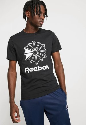 T-shirt in cotone nero con una grande grafica di una stella bianca e la parola "Reebok" in grassetto bianco sul lato anteriore. Maniche corte, scollatura rotonda.