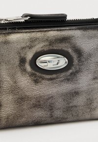 Μεταλλικό γκρι πορτοφόλι με υφή και ομαλή επιφάνεια, με κυκλικό ασημένιο λογότυπο και κλείσιμο με φερμουάρ.