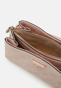 Sac bandoulière en cuir rose embossé avec fermeture éclair dorée et logo métallique triangulaire, présentant des compartiments ouverts et une doublure en tissu de marque.