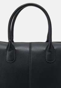 Gros plan d'un sac à main en cuir noir texturé avec deux poignées arrondies et une couture verticale au centre.