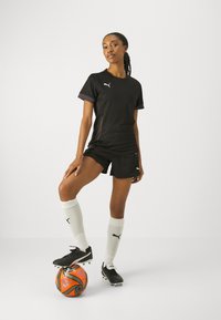Black athletic shirt and shorts. White soccer socks. Black cleats. Player standing on an orange and black soccer ball. Simple background.