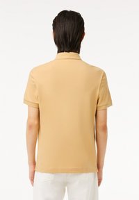 Beige kortärmad polo skjorta gjord av slät tyg med klassisk krage och uppvikt ärmved, visad från baksidan.