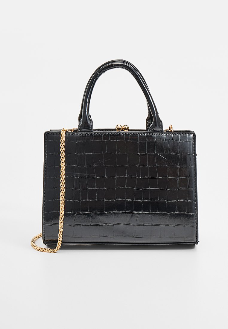 Sac à main en simili cuir noir avec une texture crocodile, bandoulière en chaîne dorée, forme structurée et poignées courtes. Fermé par un fermoir.