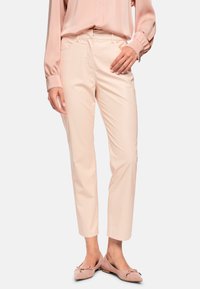 Hellrosa Hose mit geradem Schnitt, aus glattem Stoff, mit Seitentaschen und Gürtelschlaufen, kombiniert mit passenden flachen Schuhen.