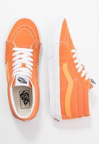Baskets montantes en daim orange avec lacets blancs, accents jaunes contrastants et semelle en caoutchouc blanche. Dispose du logo classique Vans et de détails de couture.
