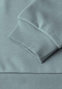 Primo piano di un tessuto di felpa blu chiaro, con polsini e orlo a costine, texture liscia con leggero allungamento.