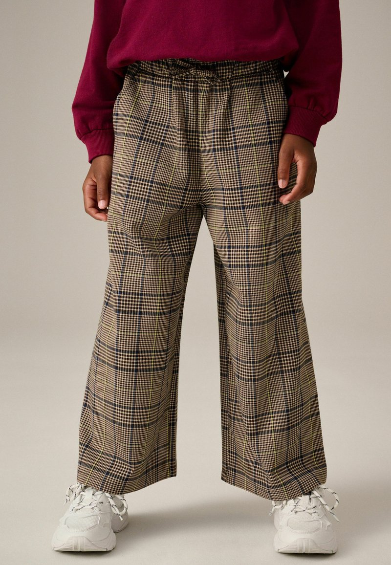 Pantaloni a gamba larga a scacchi con un motivo beige, nero e verde; vita elastica; abbinati a sneakers bianche.