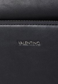 Fekete bőr kézitáska textúrázott felülettel, cipzáros záródással és fényes "VALENTINO" logó díszítéssel.