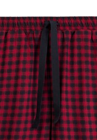 Czerwono-czarne szorty do użytku domowego w kratę, z elastycznym paskiem w talii i czarnym sznurkiem, o miękkiej bawełnianej strukturze.