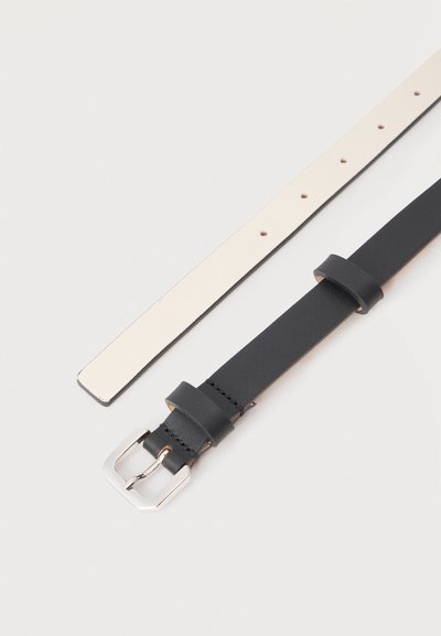 Δύο δερμάτινες ζώνες τοποθετημένες δίπλα-δίπλα, η μία μαύρη με ασημένια αγκράφα, η άλλη λευκή με πολλαπλές τρύπες για ρύθμιση.