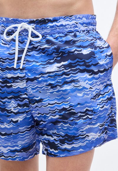 Μαγιό σορτς με μπλε κυματιστό σχέδιο, κατασκευασμένα από ελαφρύ ύφασμα. Διαθέτουν ελαστική μέση με λευκό κορδόνι και πλαϊνές τσέπες.
