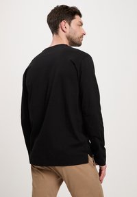 Czarny długi rękaw T-shirt wykonany z bawełny, z okrągłym dekoltem i luźnym krojem, noszony z khaki spodniami.