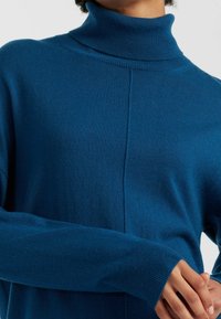 Maglione a collo alto di maglia blu scuro con una vestibilità rilassata, polsini a coste e un dettaglio di cucitura sul davanti per un tocco di texture in più.